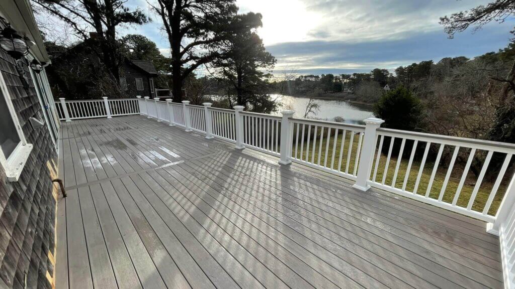 A wooden decking with white railings and a lake in the background.