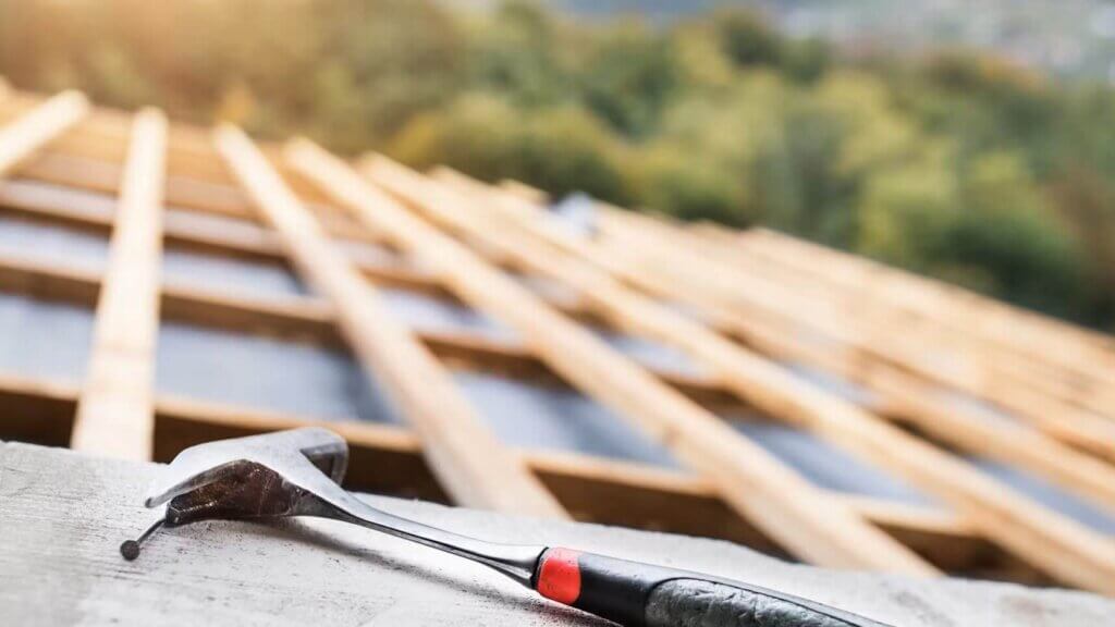 A hammer and a wrench on top of a wooden roofing.