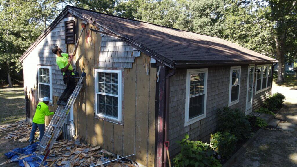 A couple of people that are standing on a ladder working on a siding.