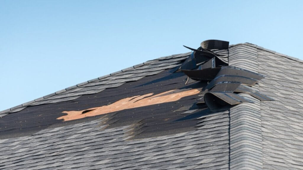 damaged black roof wih a blue sky in the background.