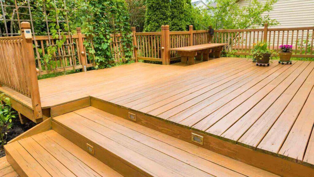 wood deck whit a bench, a wood fence, two pots of flowers and a beautiful garden behind.