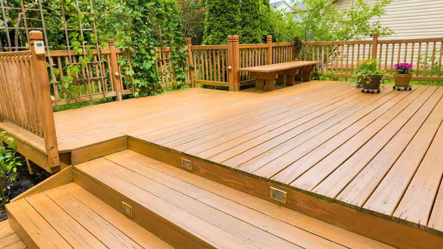 wood deck whit a bench, a wood fence, two pots of flowers and a beautiful garden behind.