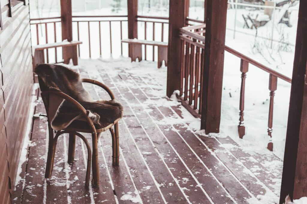 wood deck covered in snow with a wood chair and wood fence.
