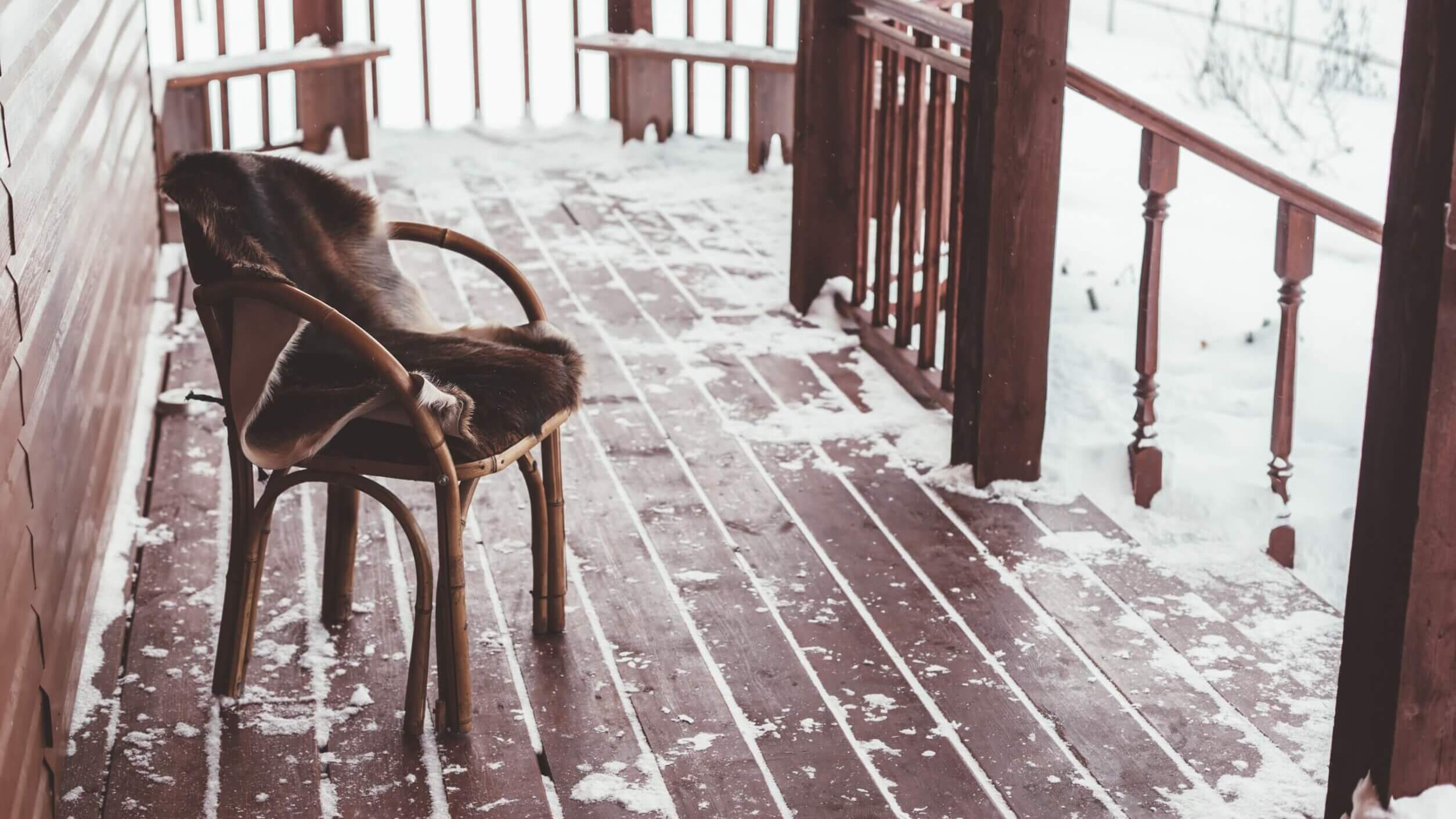 wood deck covered in snow with a wood chair and wood fence.