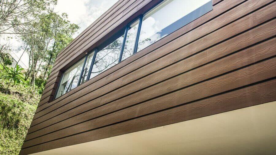 A brown siding with a window and a florest in the background.