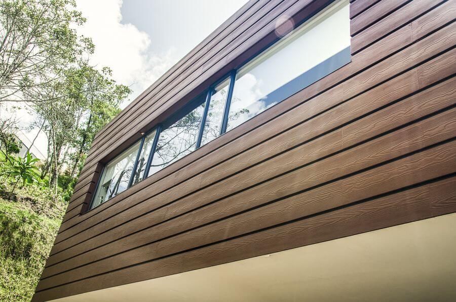 A brown siding with a window and a florest in the background.