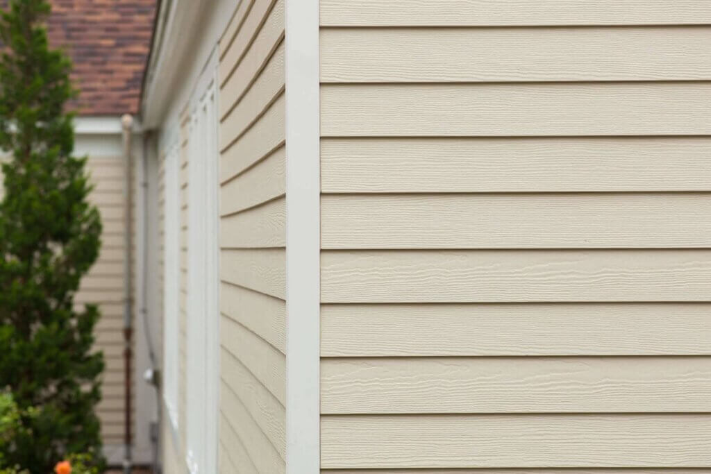 white vinyl siding of a house with tree in the left part of the background.